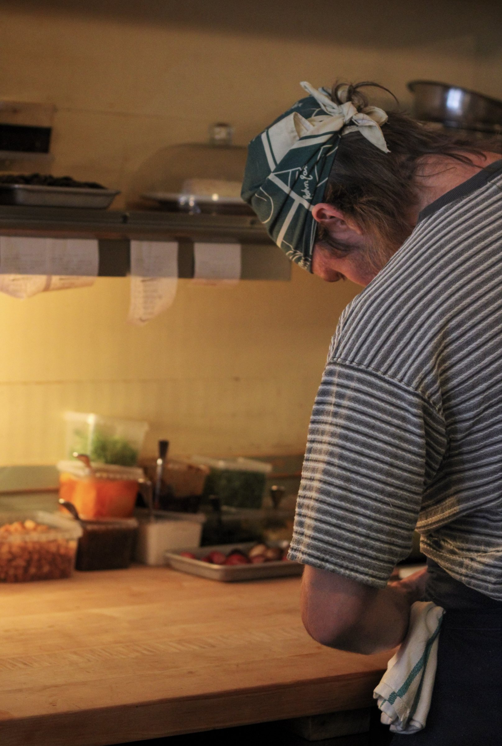 A cook in profile, bandana tied back, pausing over the counter