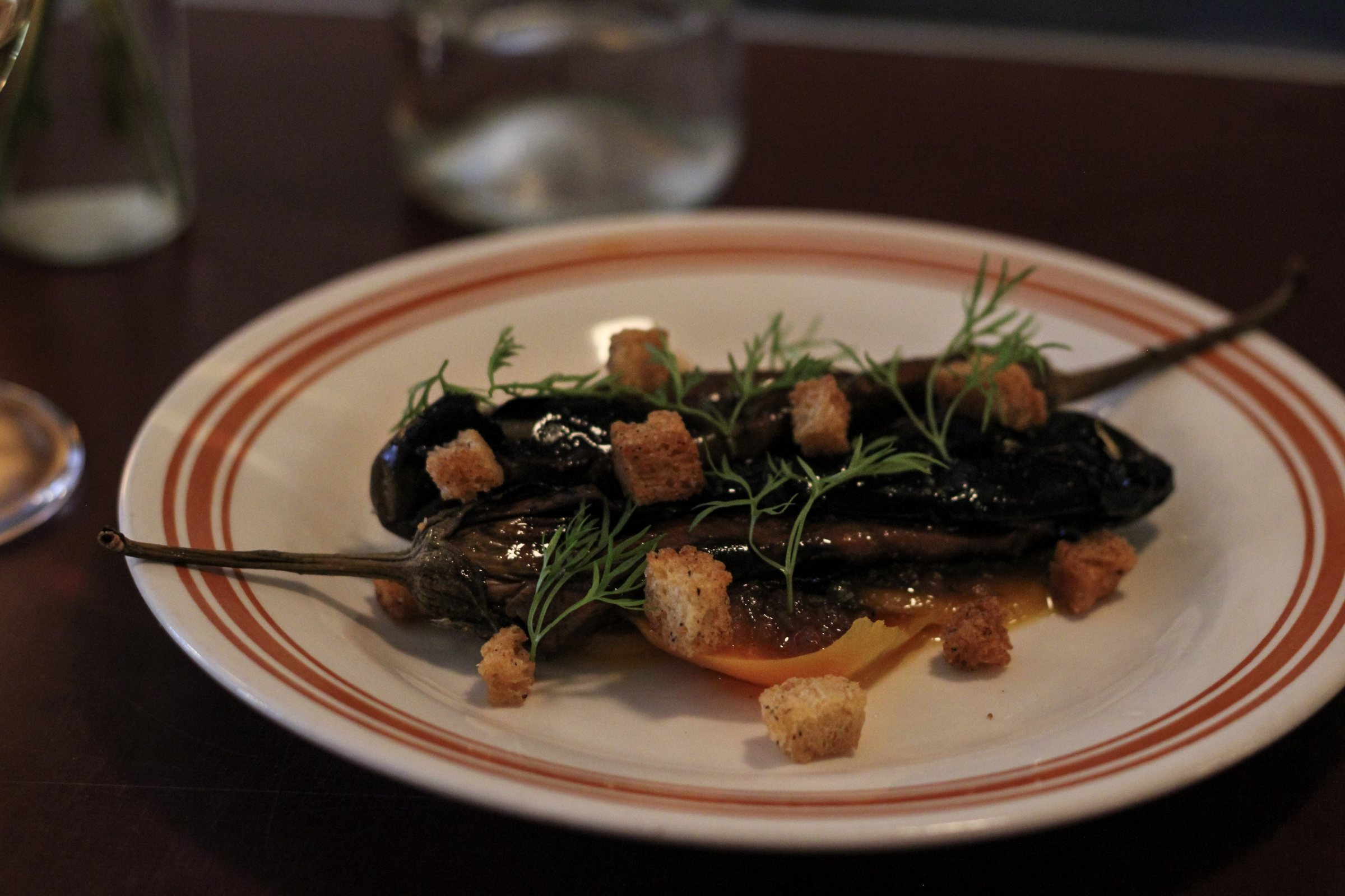 Charred eggplant with croutons and dill over a bright orange sauce
