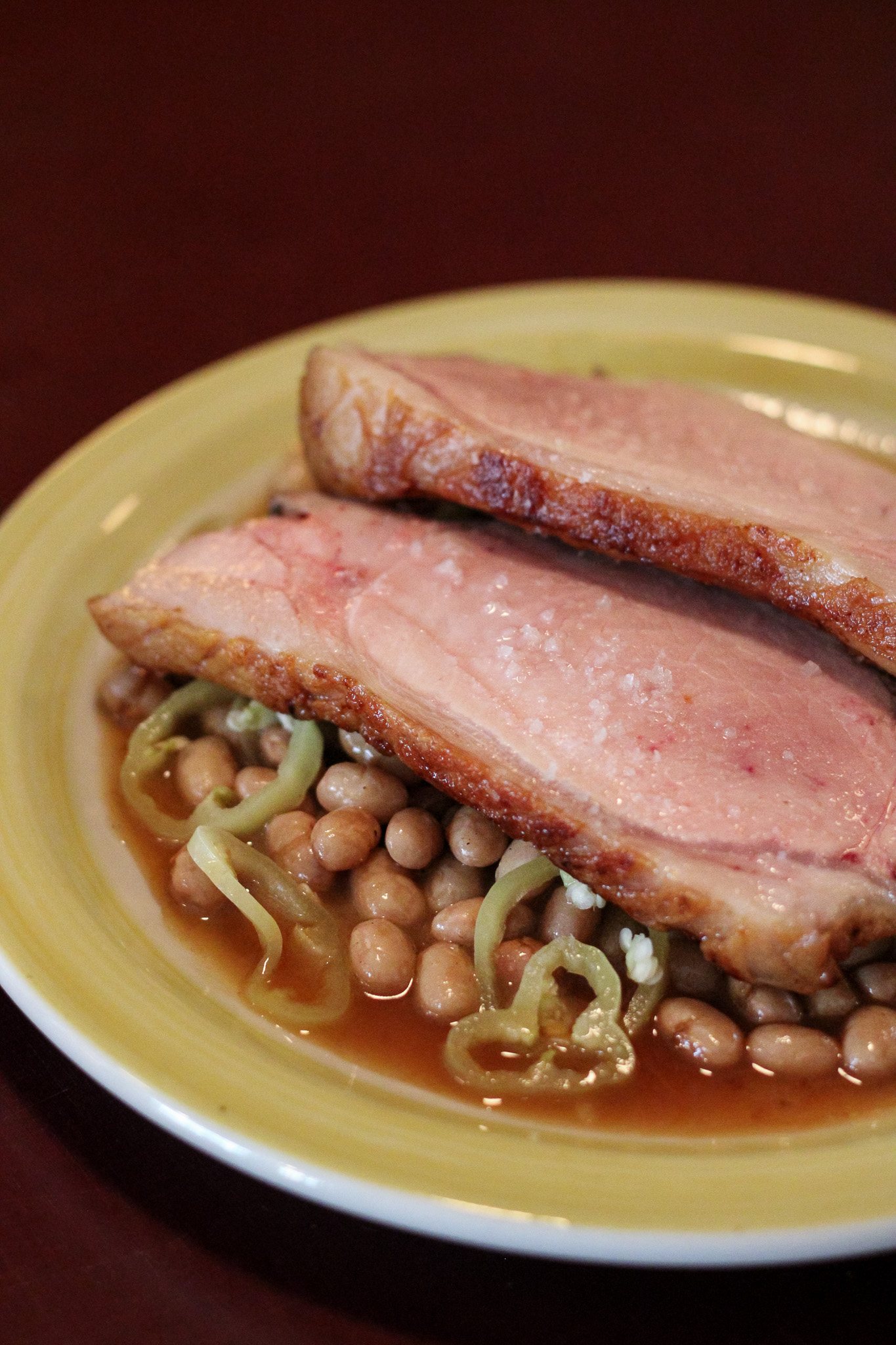 Sliced pork over beans and pickled peppers on a yellow plate
